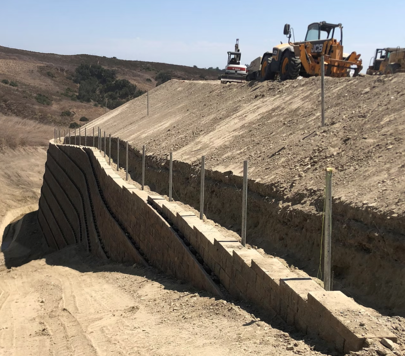 industrial size retaining wall on a slope with an excavator at top of slope