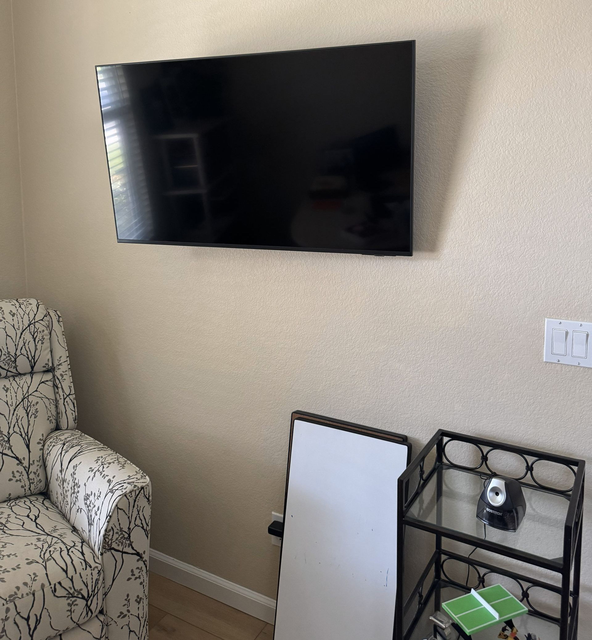 Person in green sweater assembles wooden stool with a screwdriver in a workshop.
