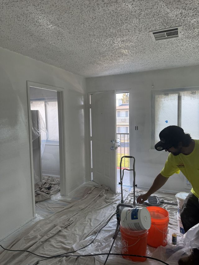 Bedroom with bed, desk, window, and rug. Gray walls, dark blue curtains, and light-colored bedspread.