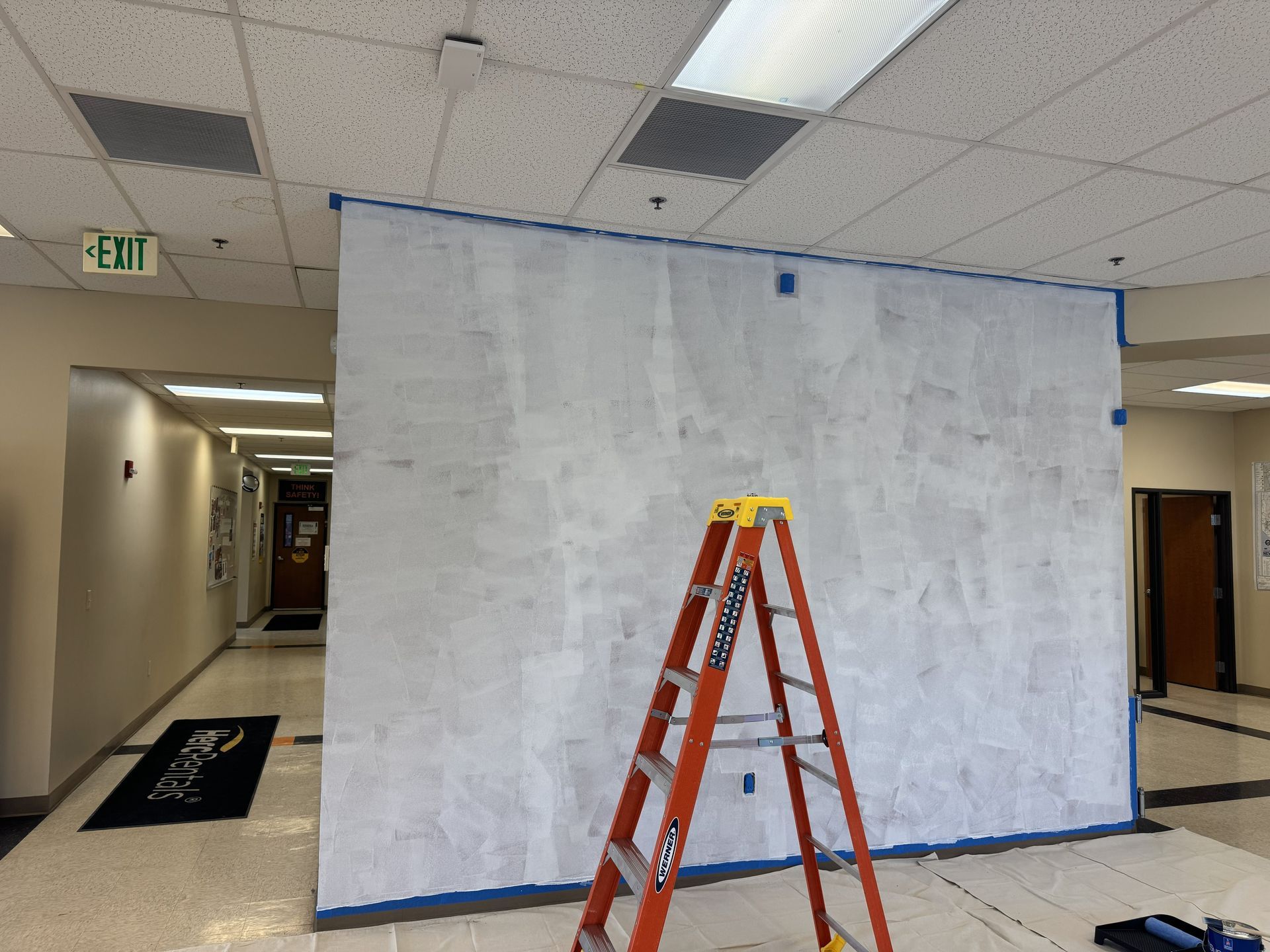 Wooden step ladder with paint splatters, near paint supplies and a tarp in a room being painted.