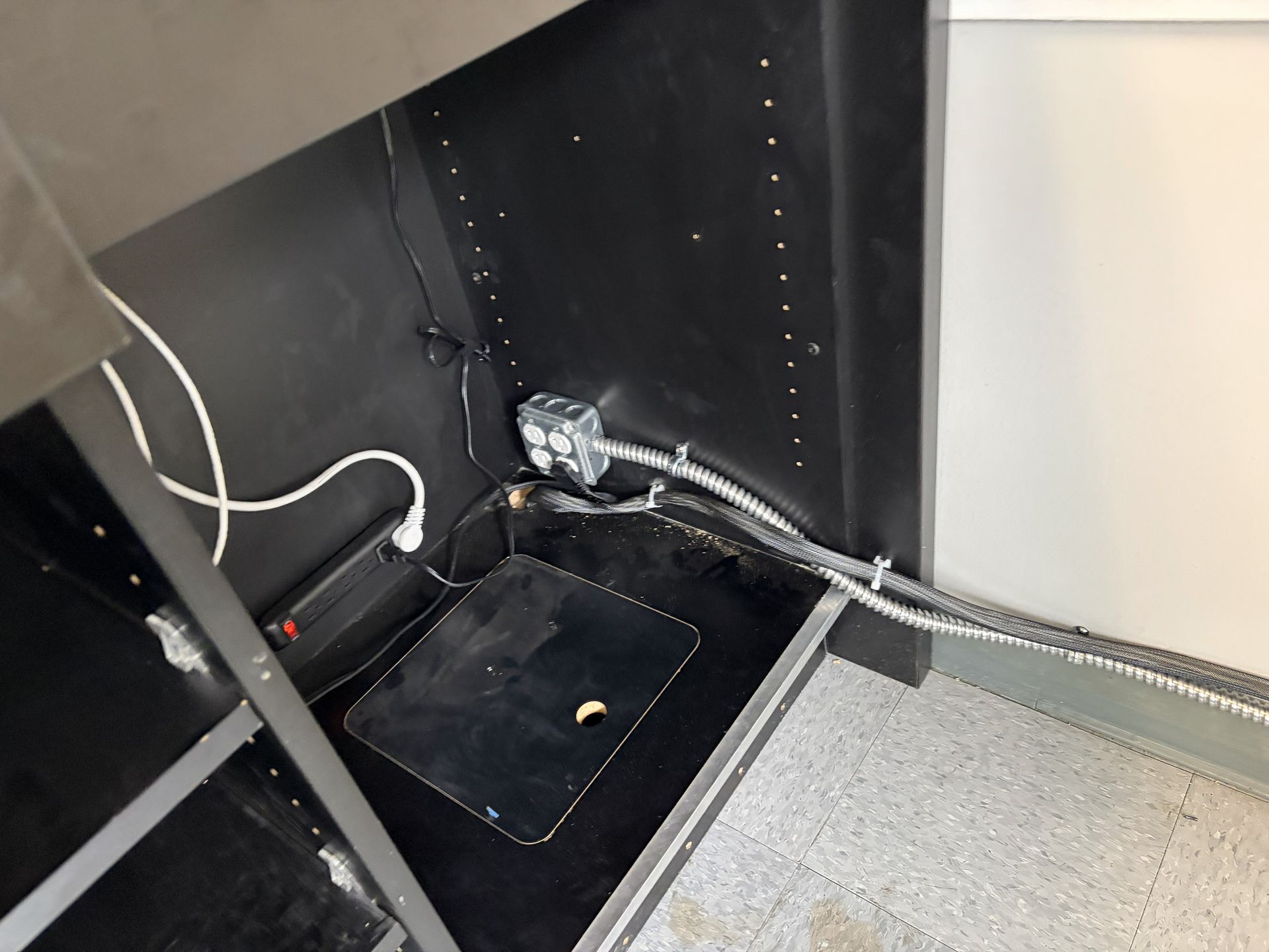 Person uses a power drill to attach a hinge to a white window frame on a wooden surface.