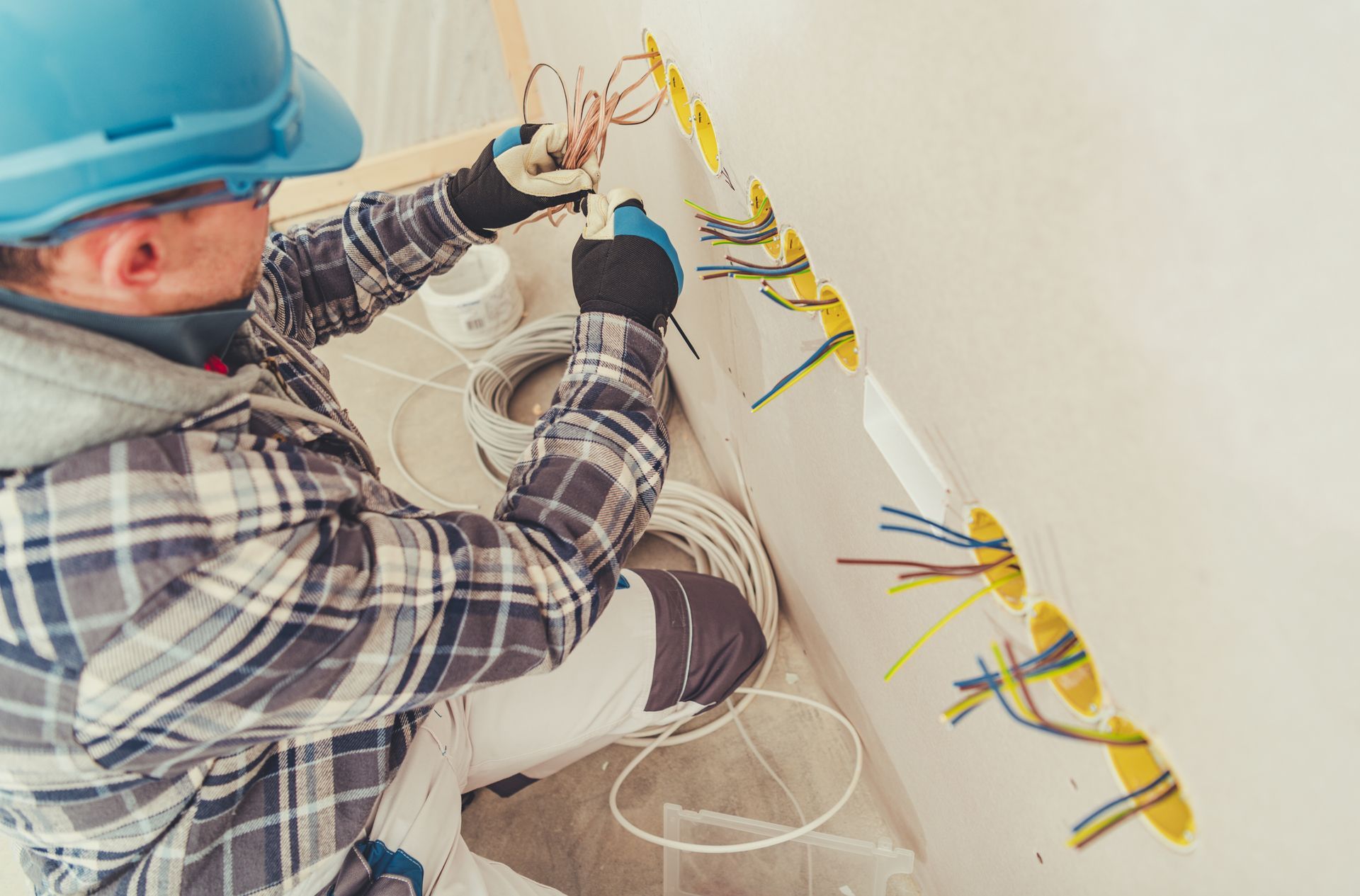 Close-up of a commercial electrician, wearing a blue helmet and dark gloves, installing outlets.