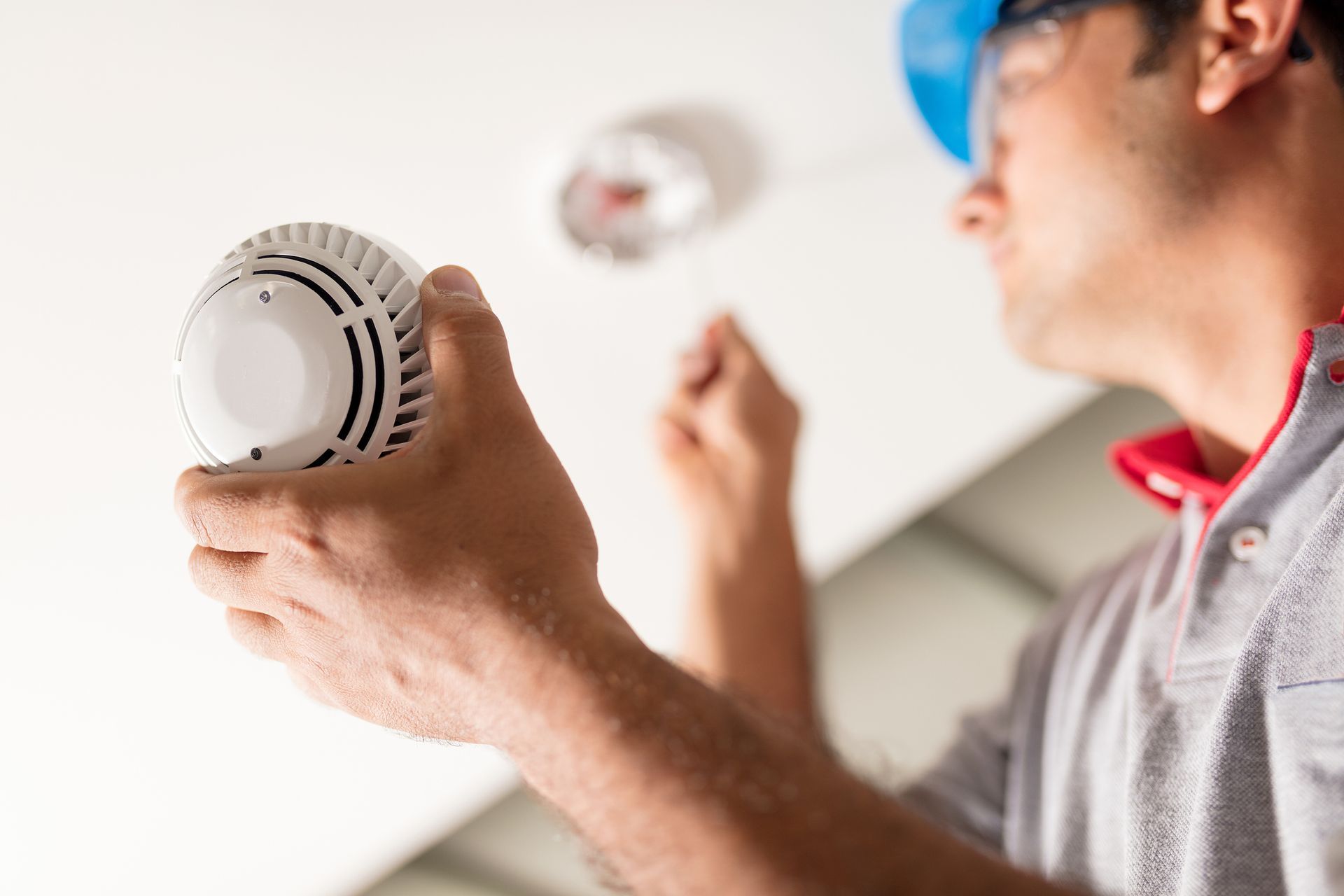 Person installing a smoke detector on a white ceiling.