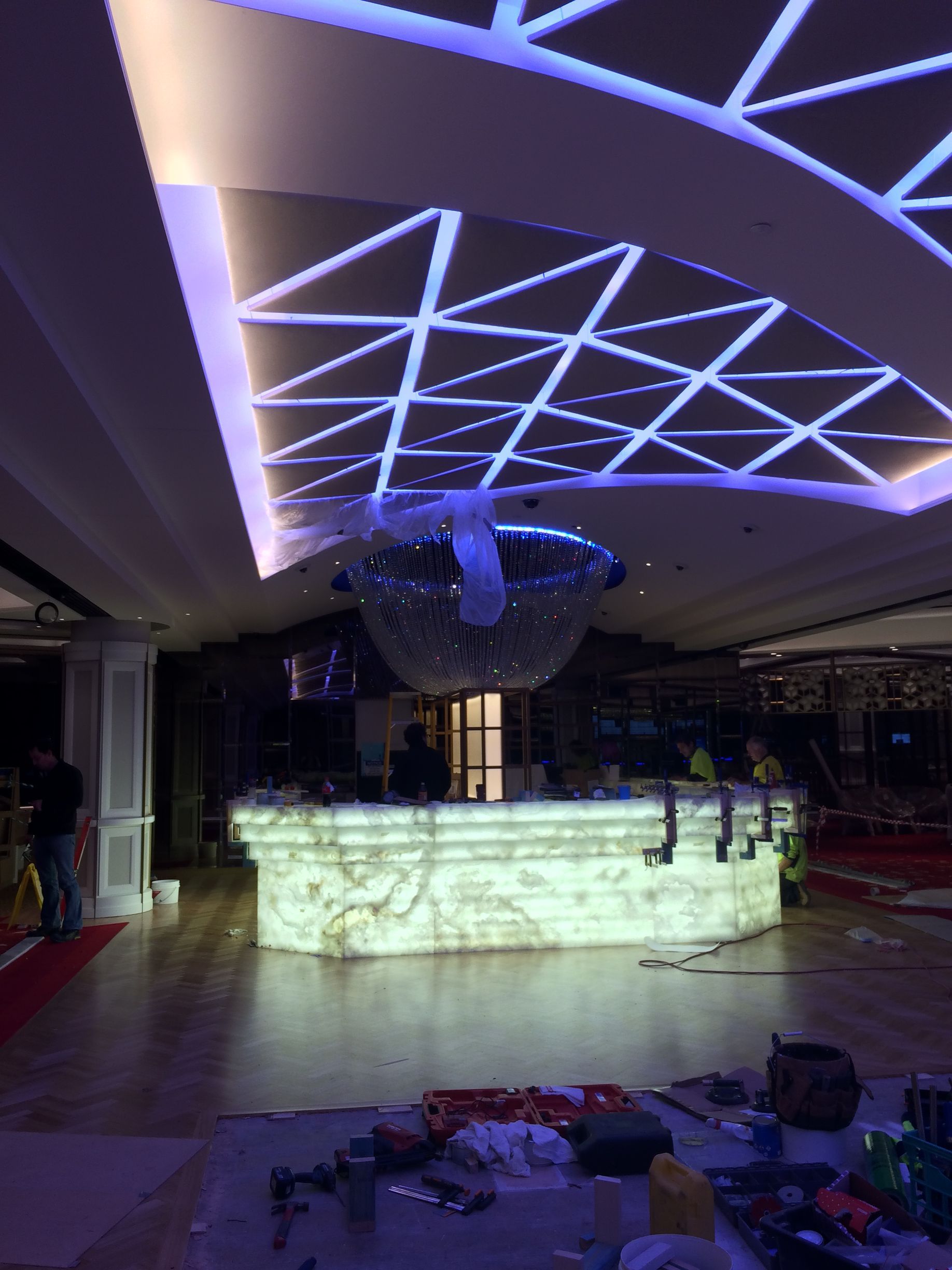 A backlit bar with an illuminated ceiling, under construction. Blue and white lighting dominates the scene, with workers present.