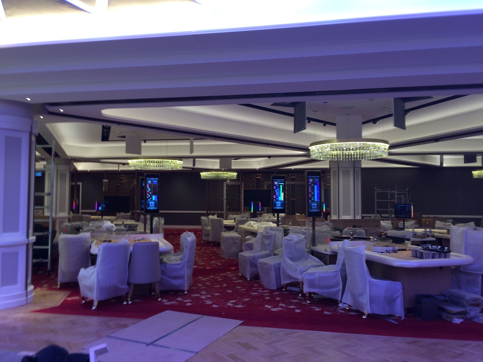 Interior of a casino under construction, with red carpet, covered furniture, and overhead lighting.
