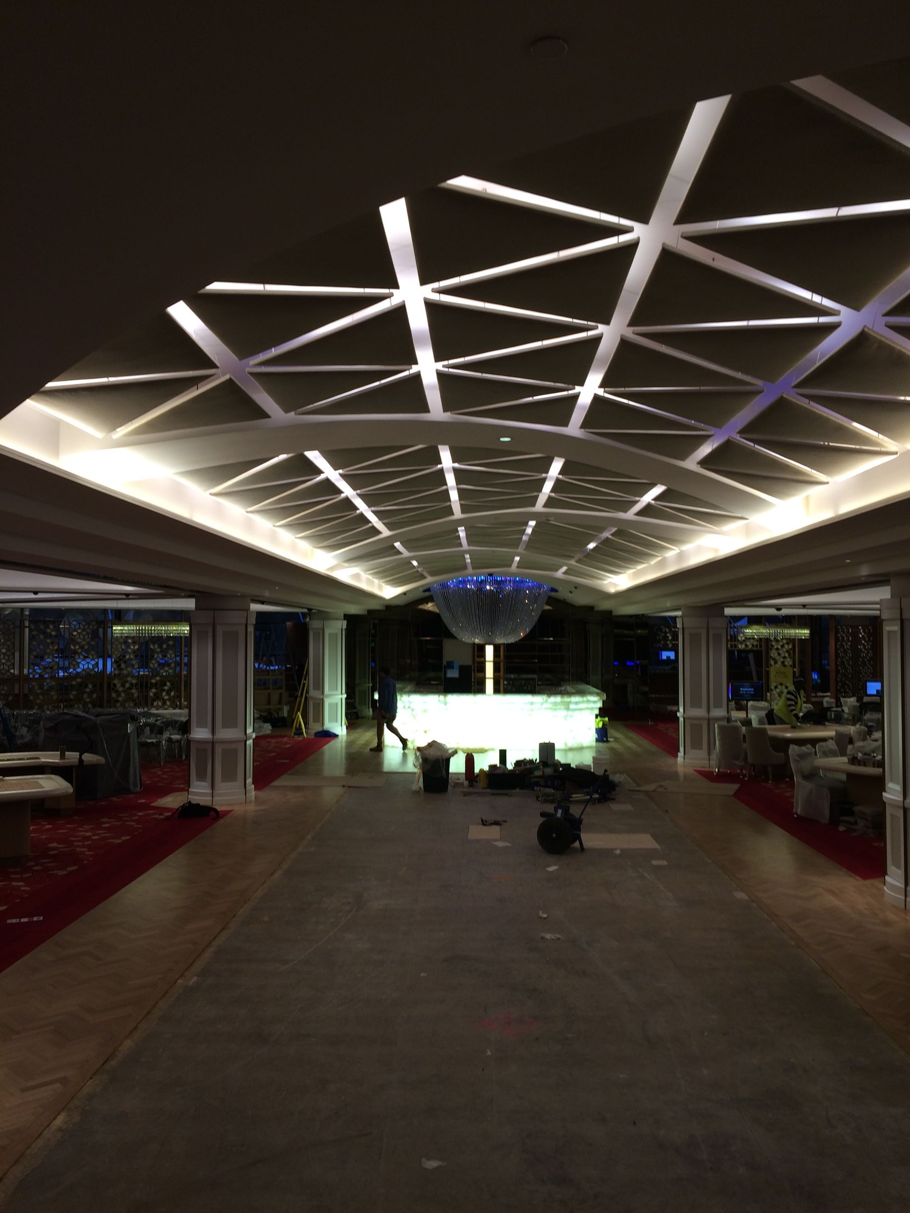 Long, modern hallway with geometric ceiling lights, leading to a glowing bar in the distance.
