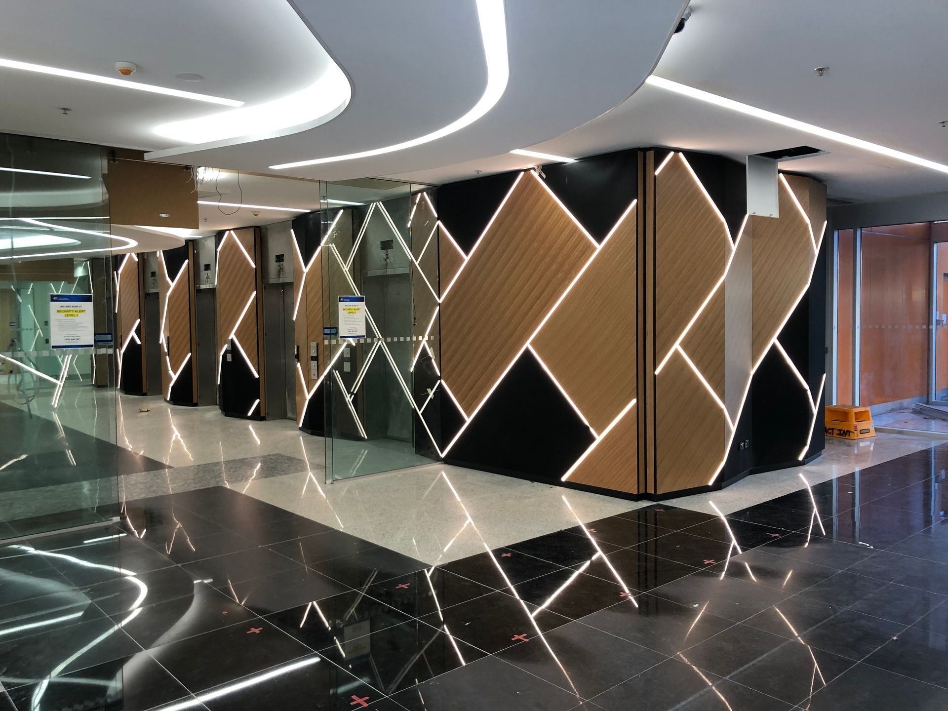 Elevator lobby with black, brown, and white geometric paneling. Fluorescent lights reflect on the glossy floor.