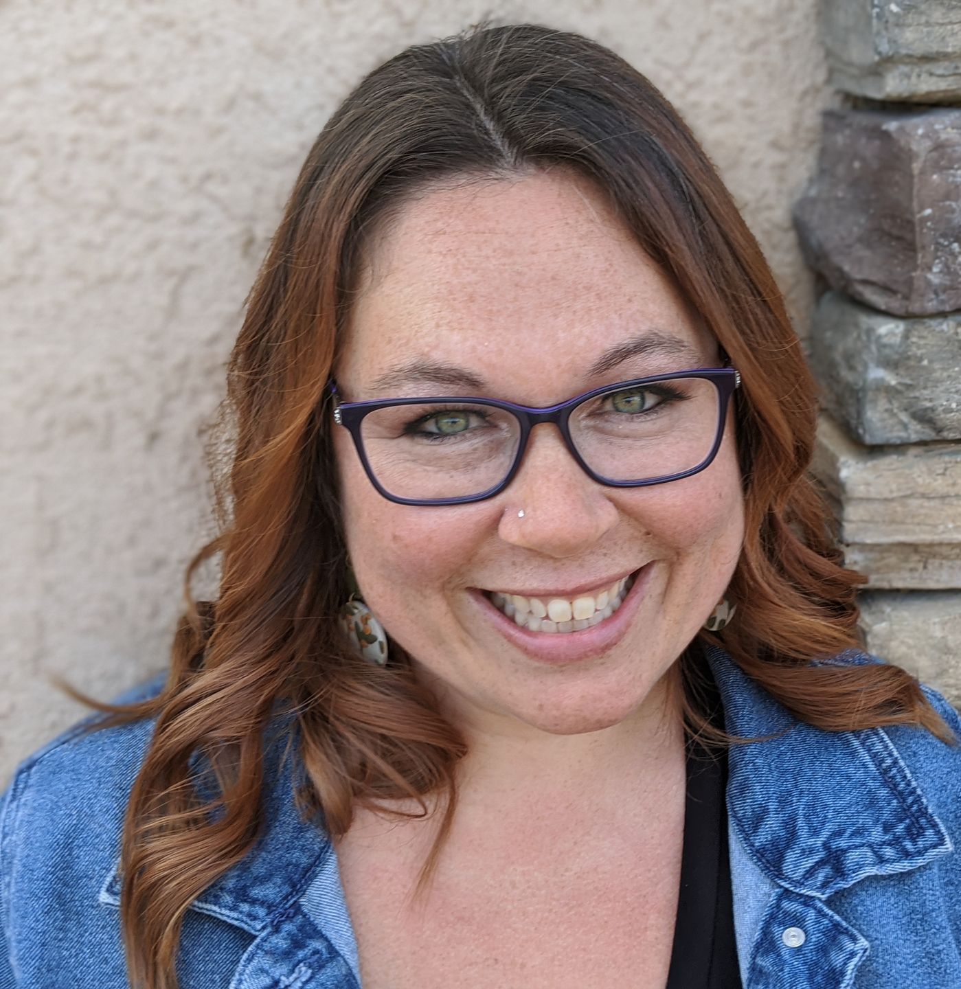 Roya Dedeaux wearing glasses and a denim jacket is smiling.