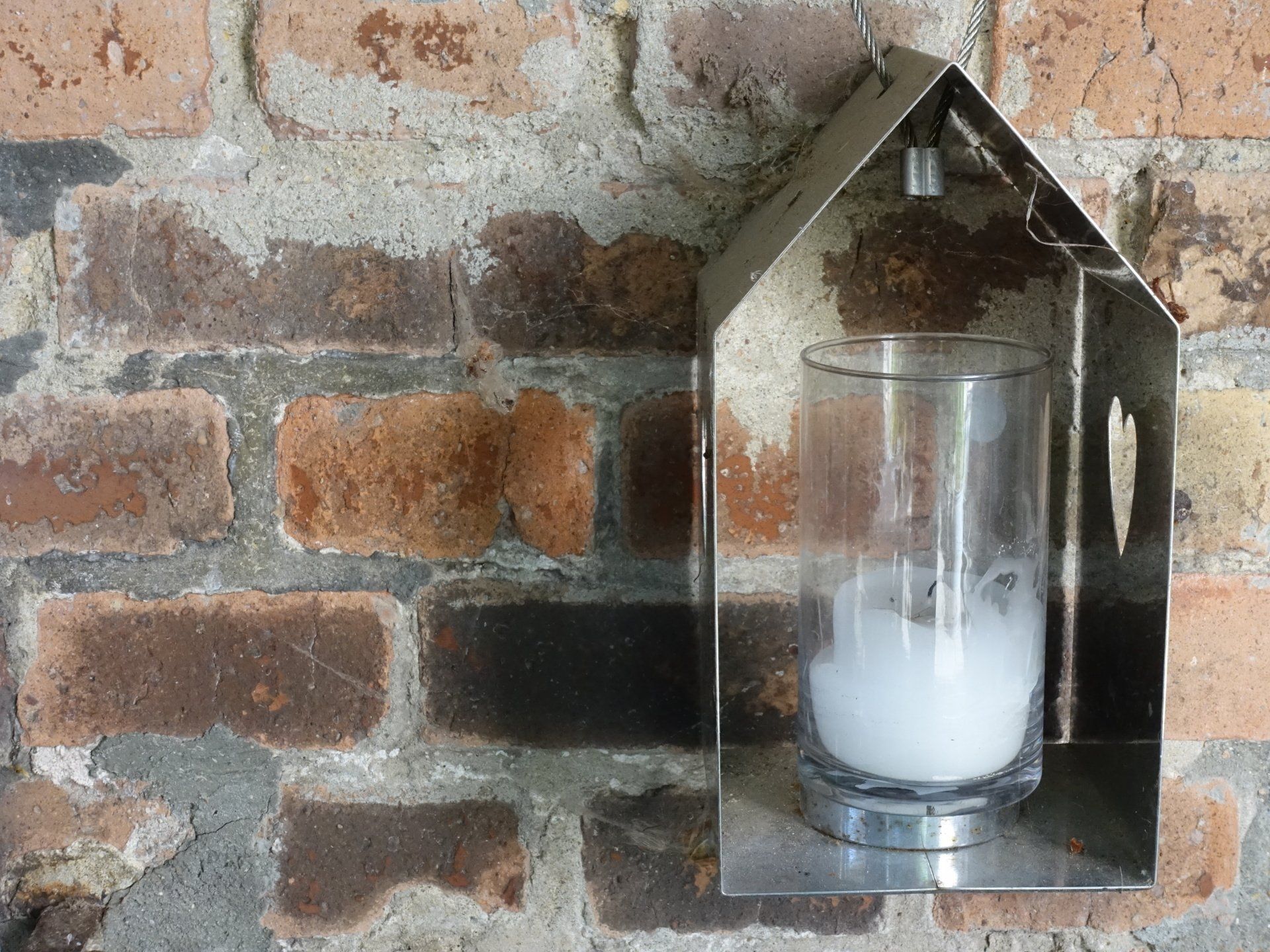 Ein Glas mit einer Kerze darin hängt an einer Ziegelwand