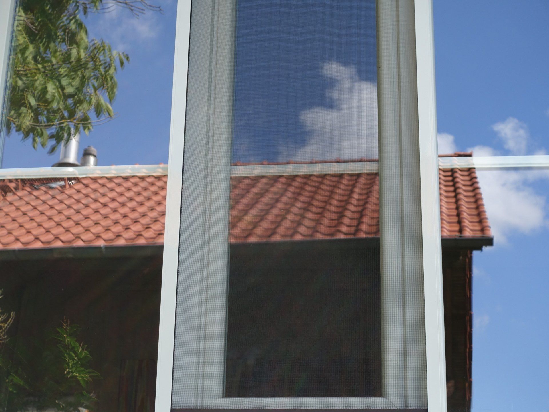 Ein Haus mit einem roten Ziegeldach und einem weißen Fenster mit einem Fliegengitter.