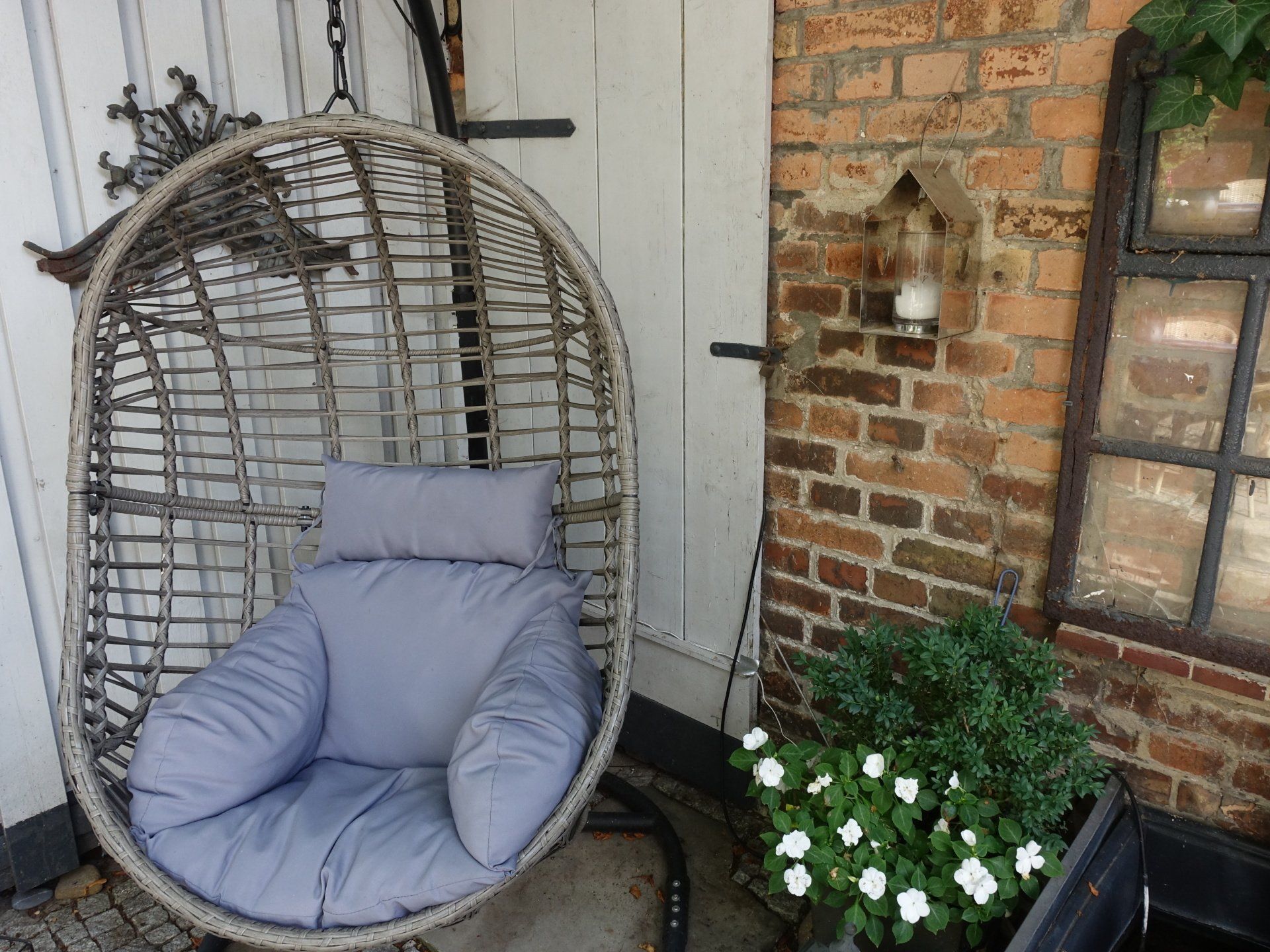 Vor einer Backsteinmauer steht ein Korbstuhl mit grauem Kissen.