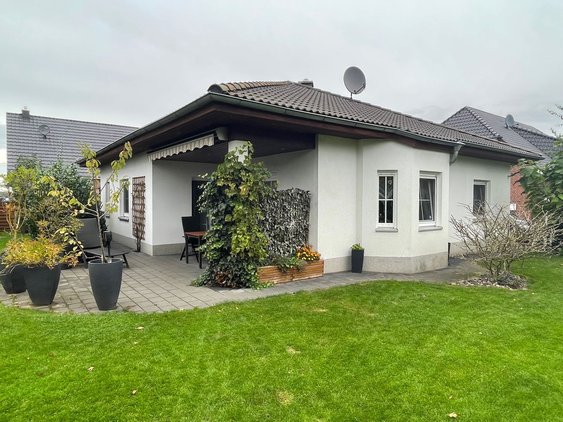 Ein weißes Haus mit einem braunen Dach und einer Terrasse davor.