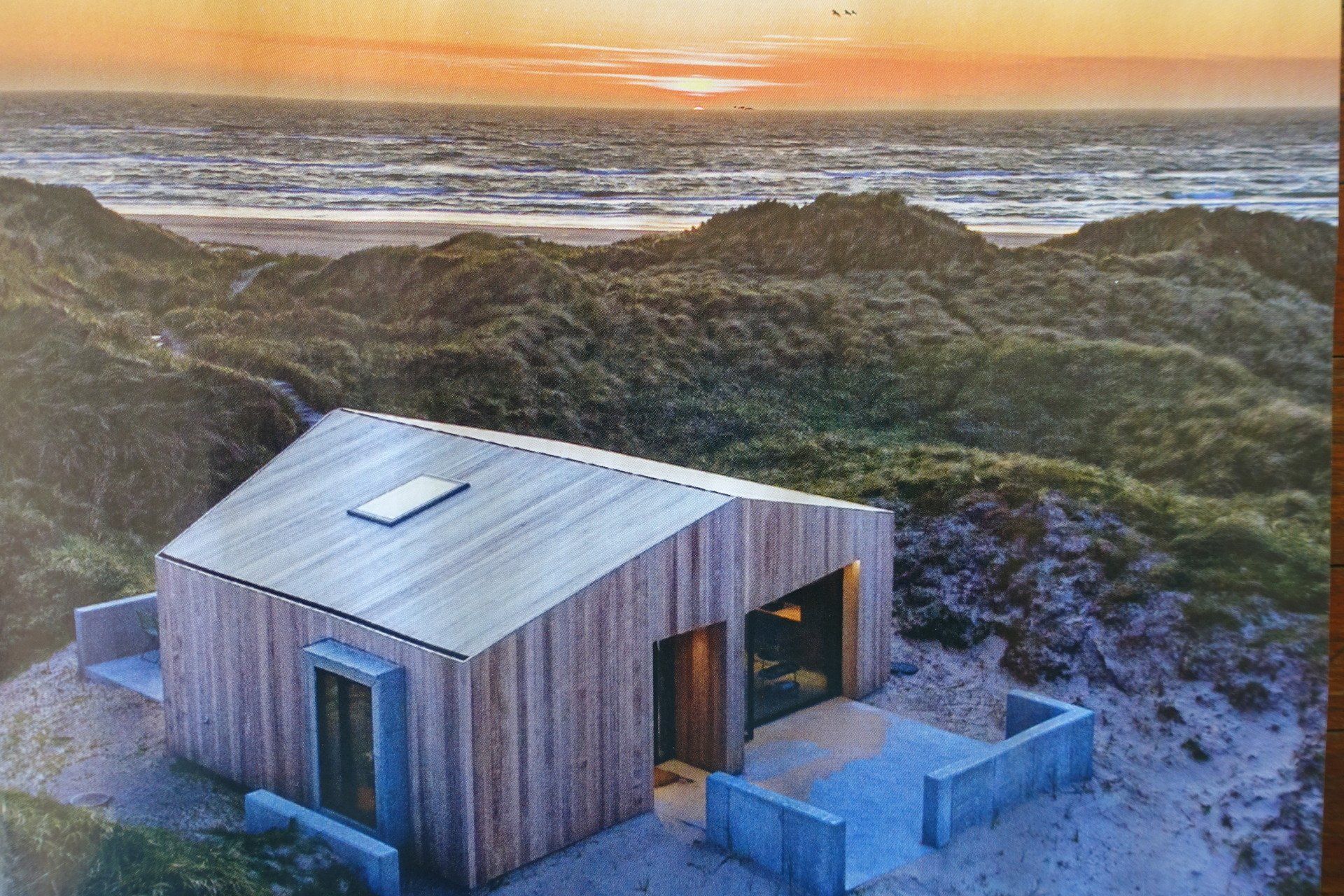 Auf einem Hügel neben dem Meer steht ein kleines Holzhaus.