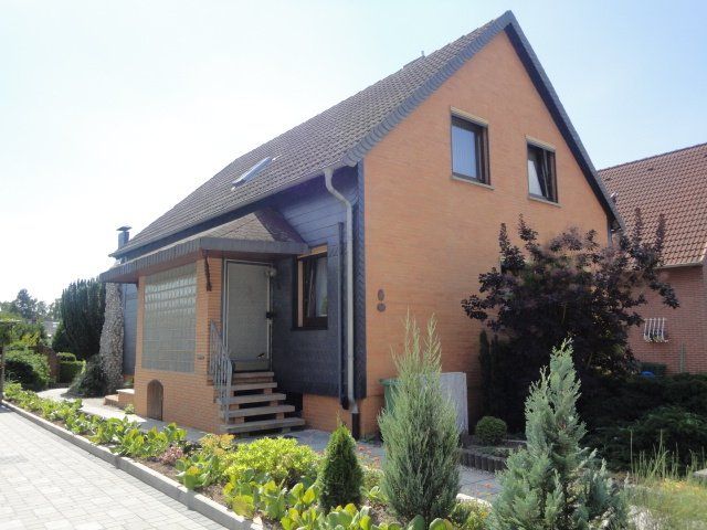 Ein orangefarbenes Haus mit schwarzem Dach ist von Bäumen und Büschen umgeben