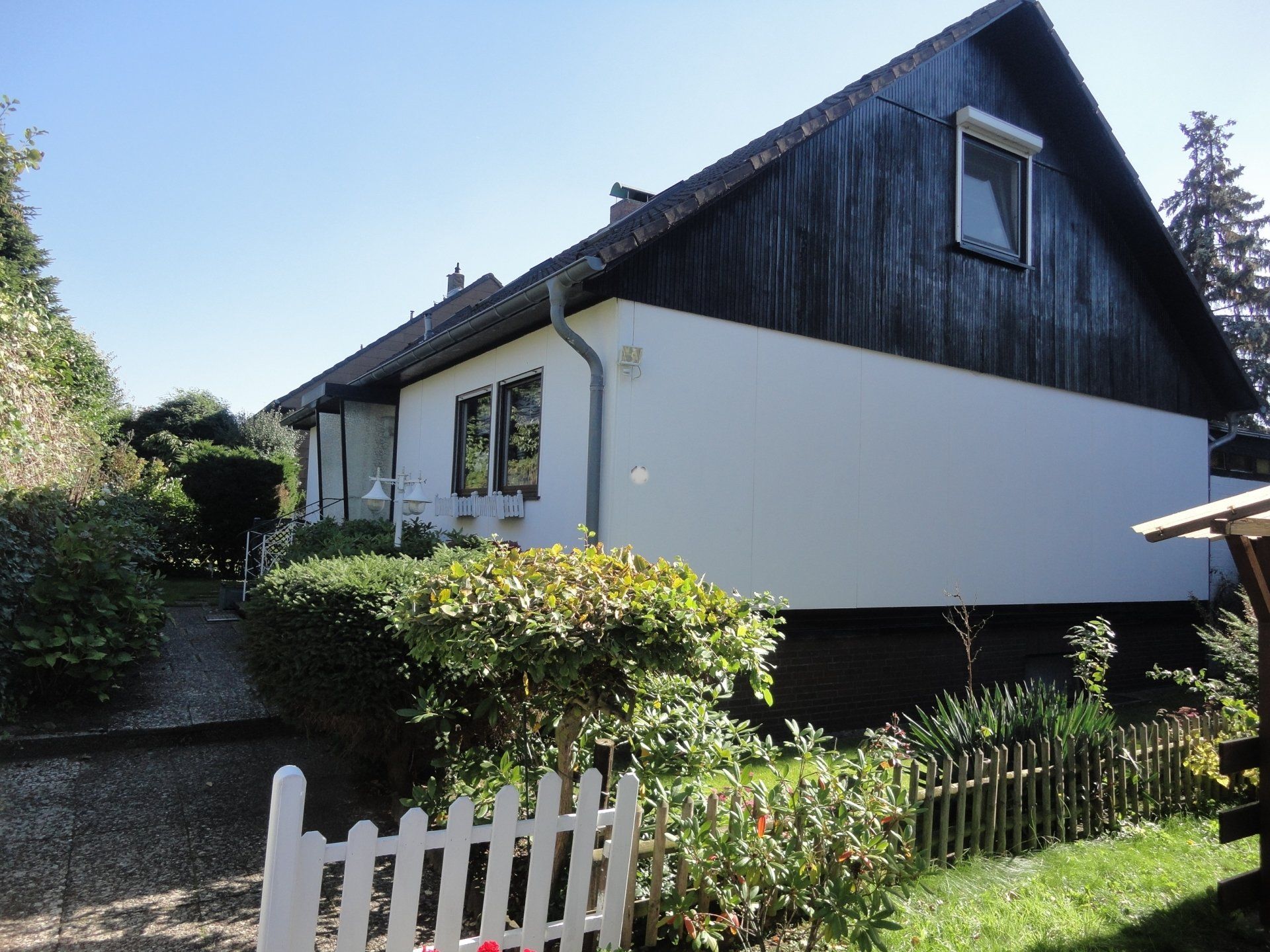 Ein weißes Haus mit einem schwarzen Dach und einem weißen Lattenzaun
