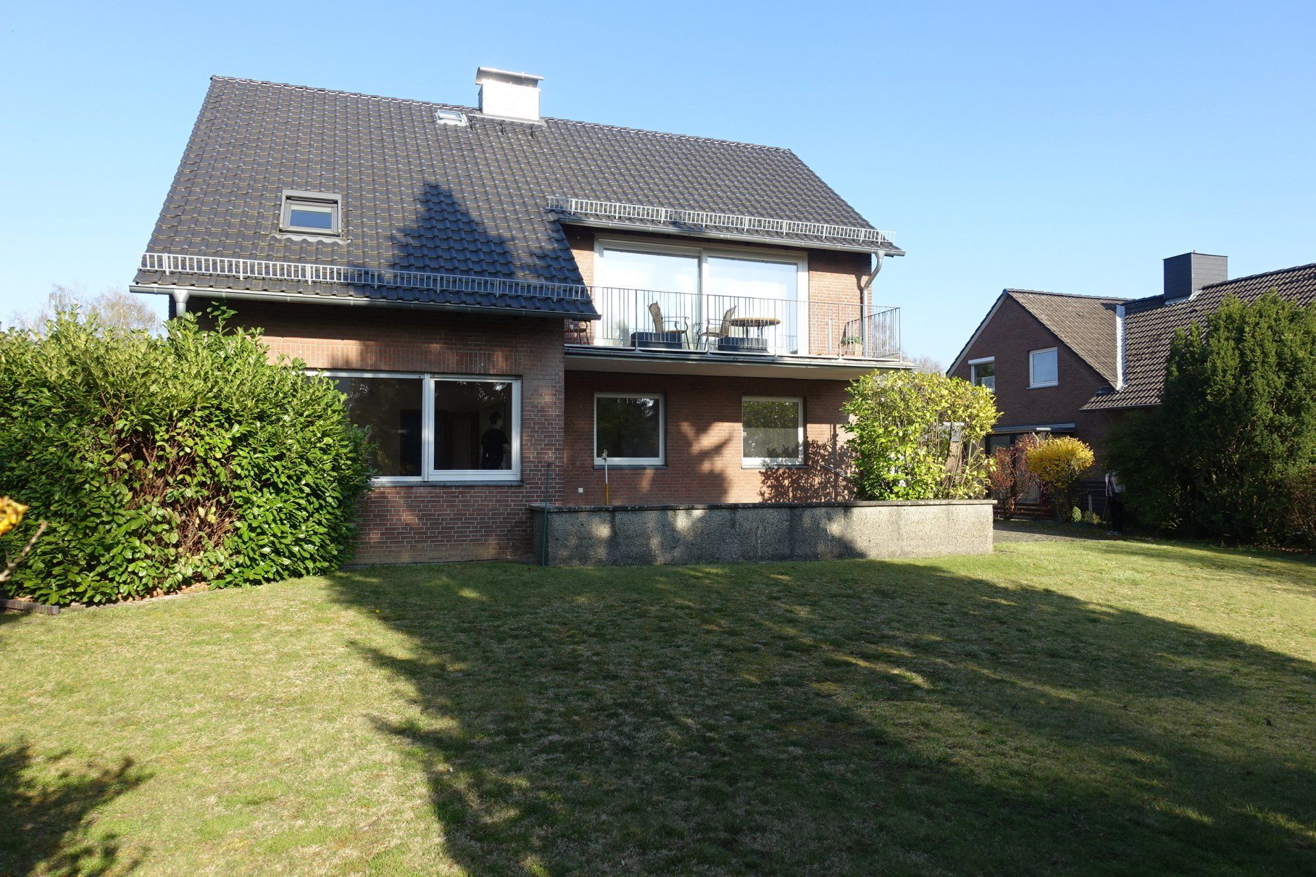 Ein großes Backsteinhaus mit schwarzem Dach und einer großen Rasenfläche davor.