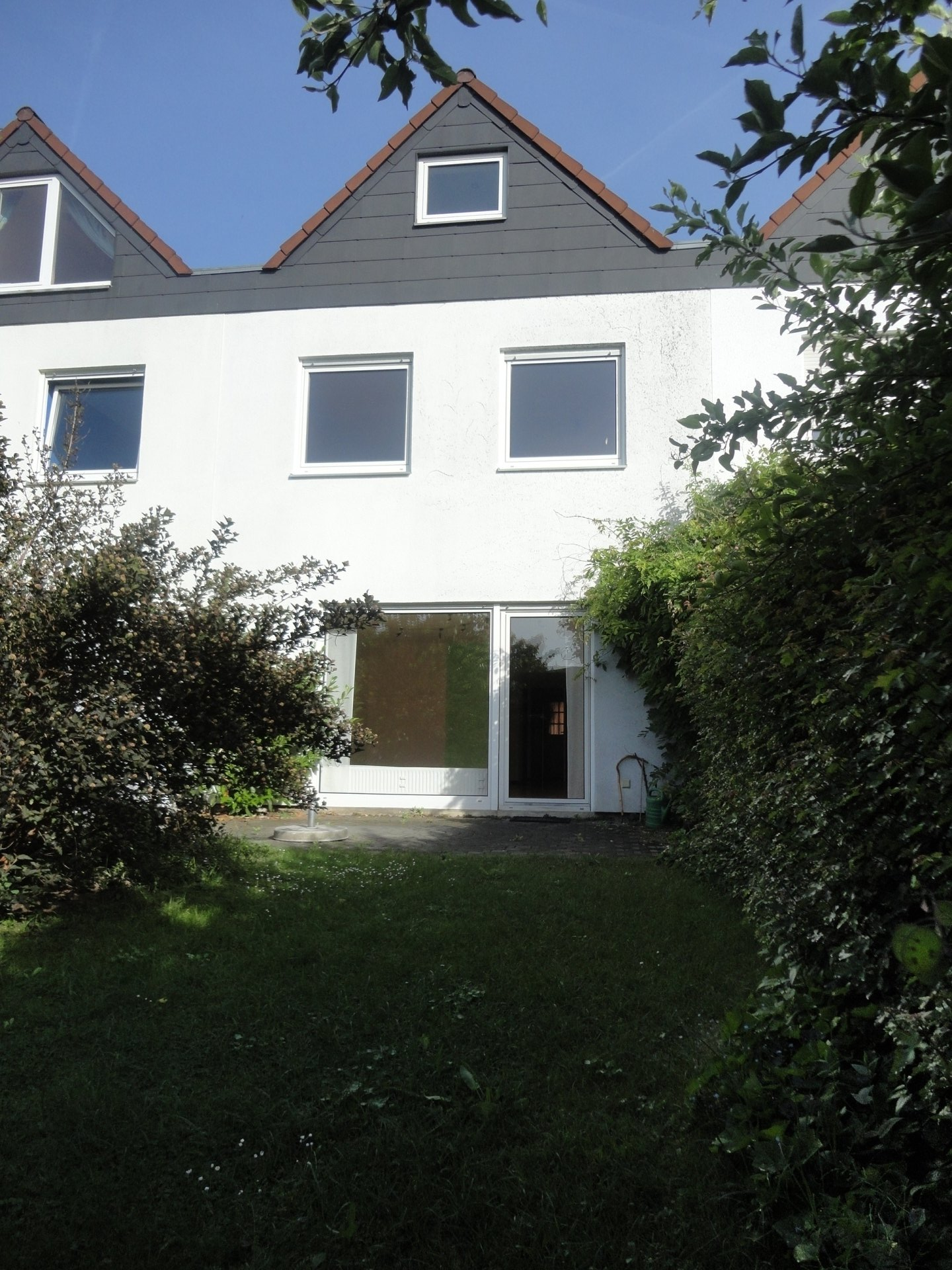 Ein weißes Haus mit Schieferdach ist von Bäumen und Büschen umgeben