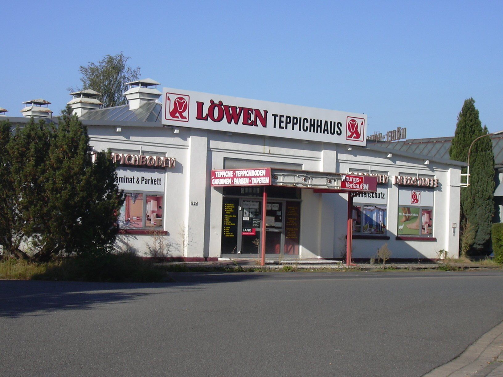 Ein weißes Gebäude mit einem roten Schild mit der Aufschrift Löwen Teppichhaus
