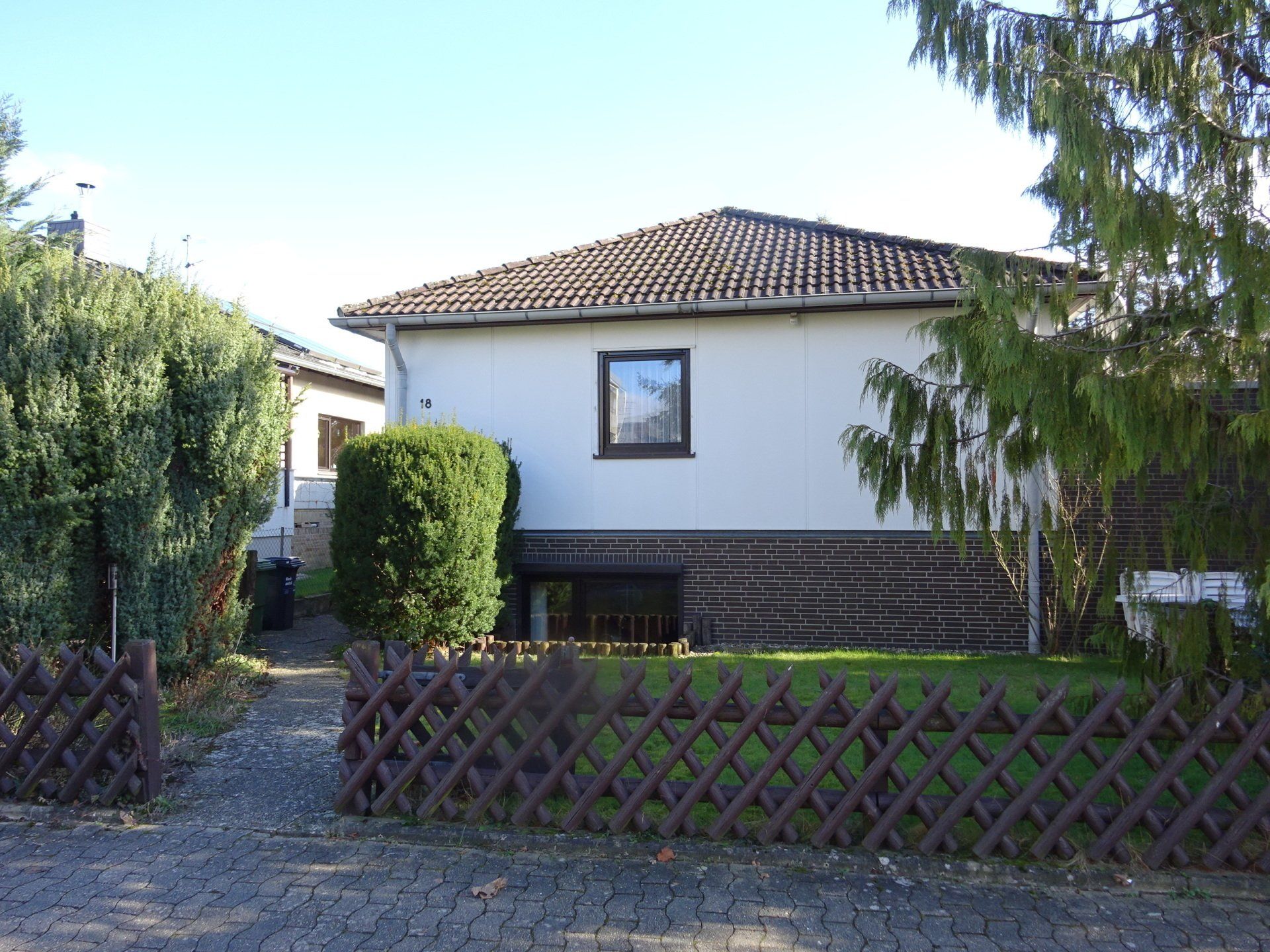 Hinter einem Holzzaun steht ein weißes Haus mit braunem Dach