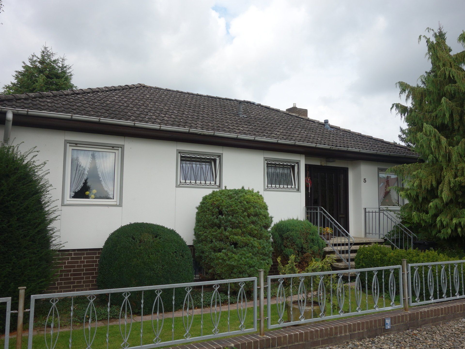 Ein weißes Haus mit einem braunen Dach und einem Zaun davor