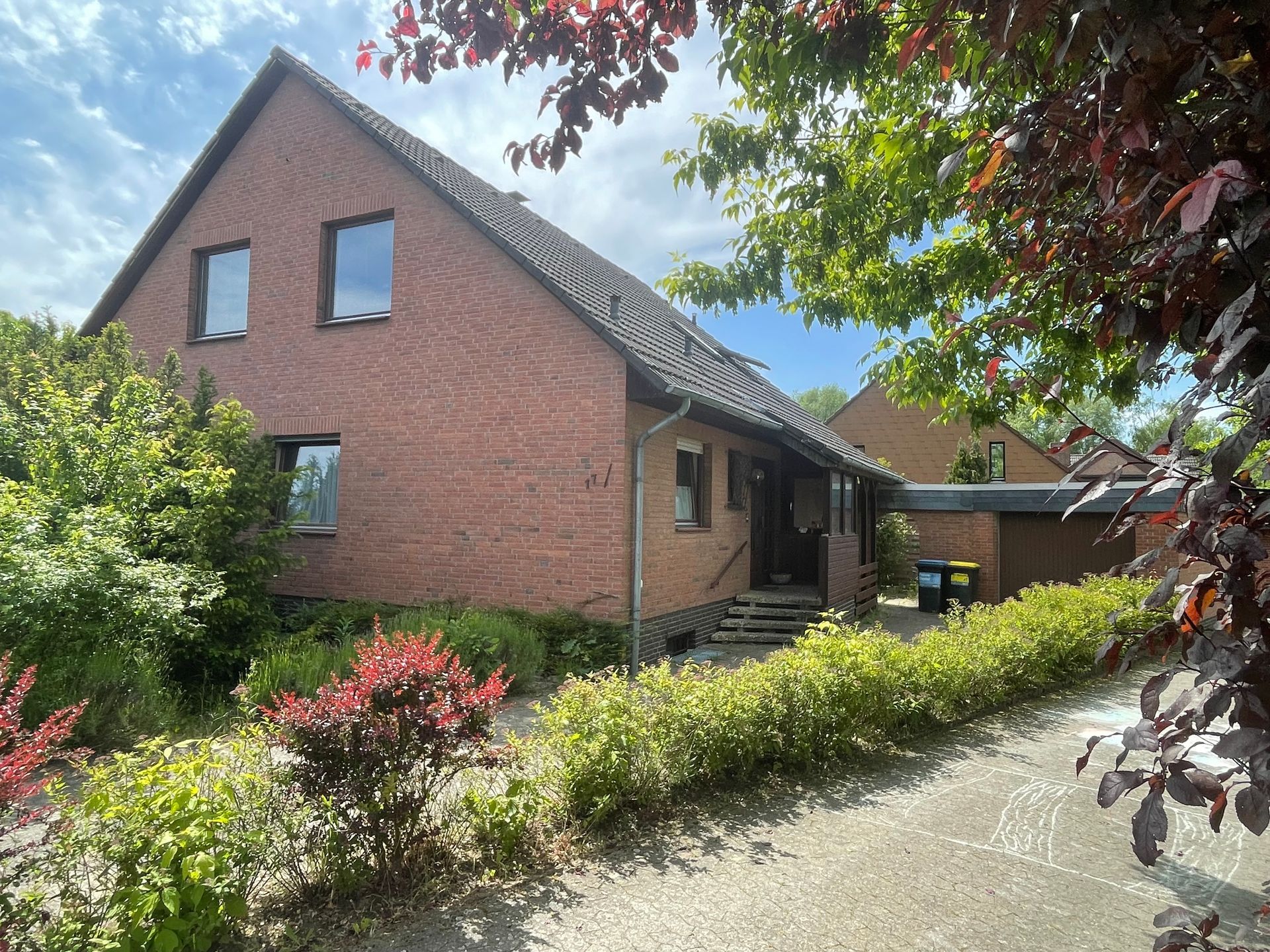 Ein Backsteinhaus mit Garage und Auffahrt ist von Büschen und Bäumen umgeben.