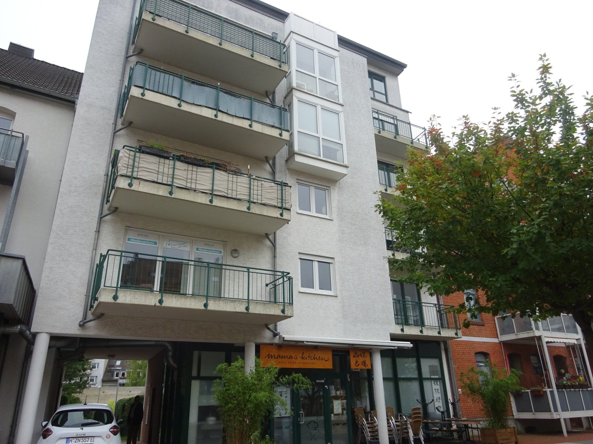 Ein weißes Gebäude mit Balkonen und einem davor geparkten Auto