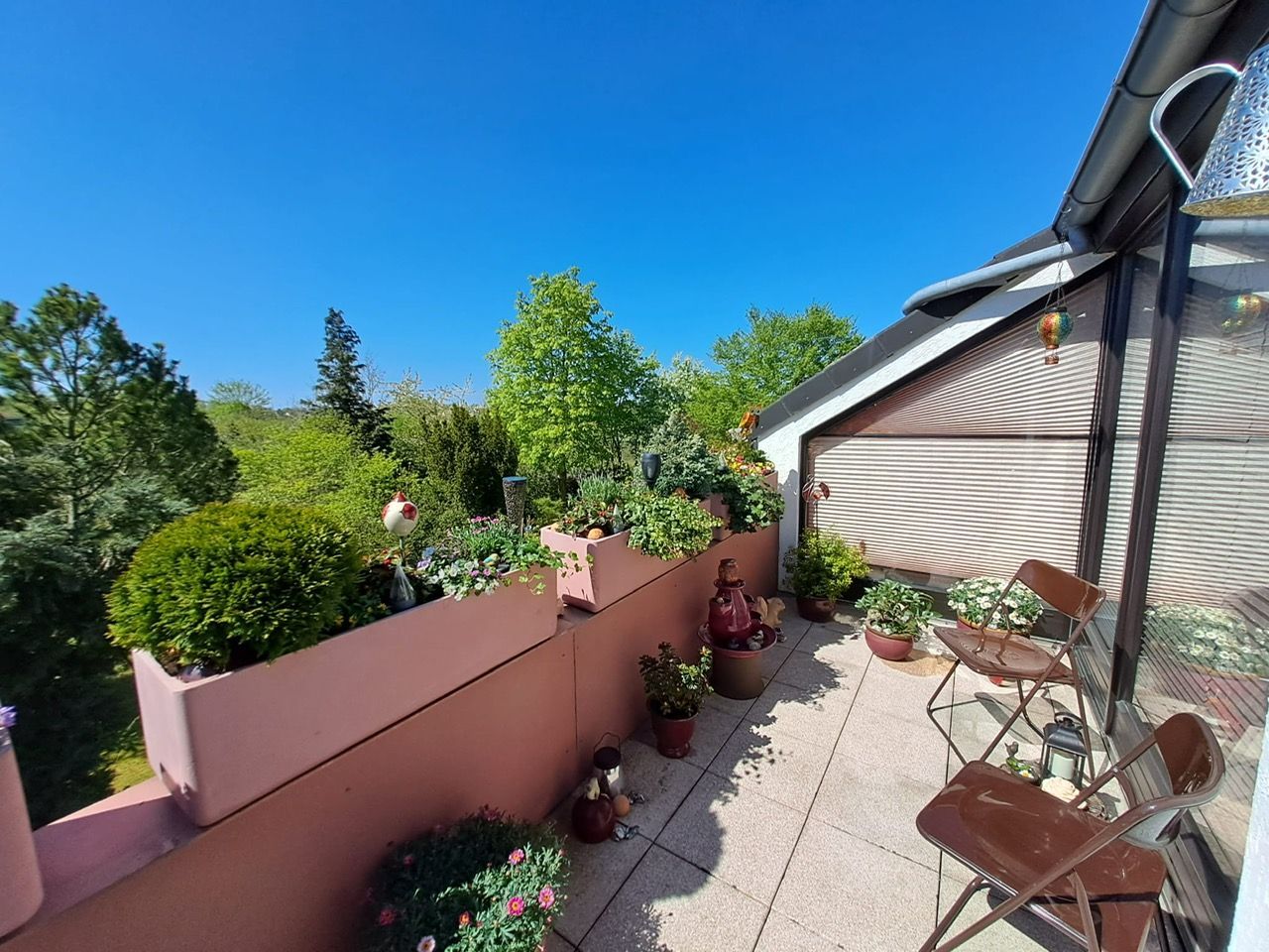 Ein Balkon mit Stühlen, Tischen und Topfpflanzen an einem sonnigen Tag.