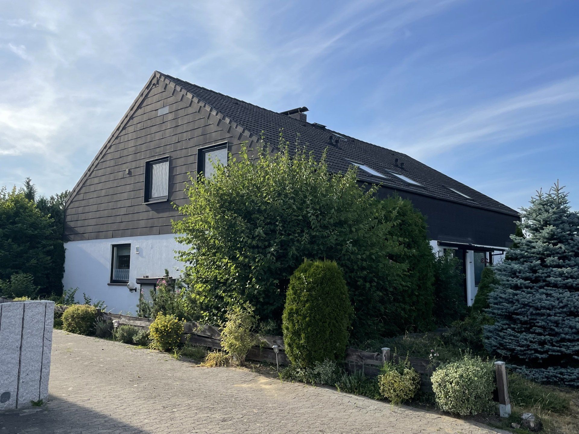 Ein weißes Haus mit schwarzem Dach ist von Bäumen und Büschen umgeben.