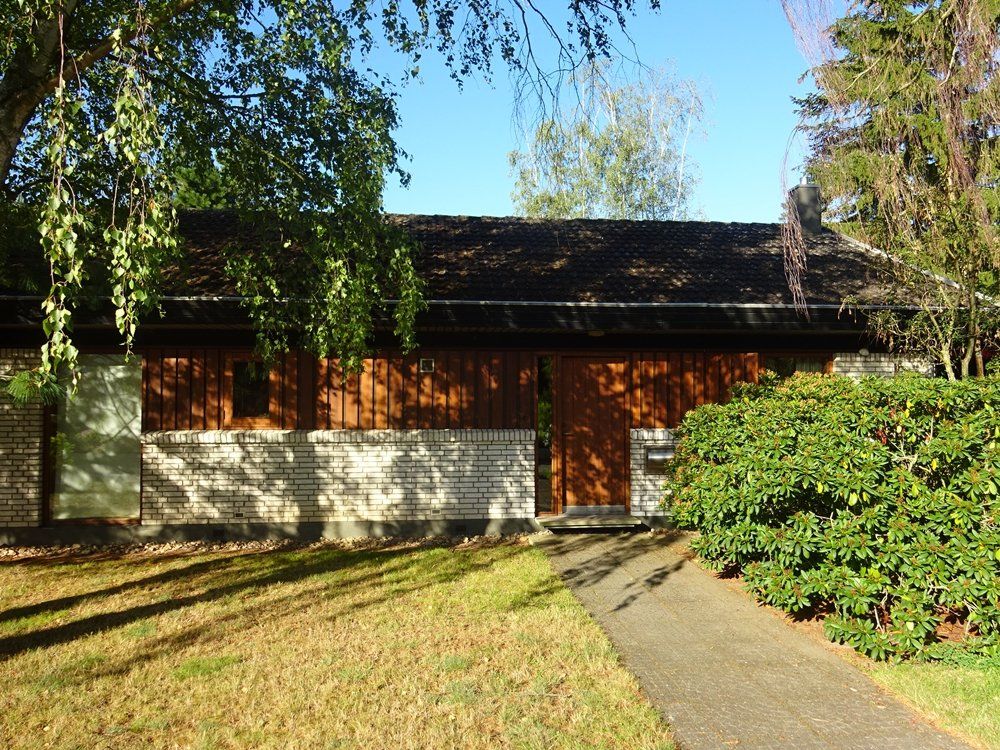 Ein Haus mit schwarzem Dach ist von Bäumen und Gras umgeben.