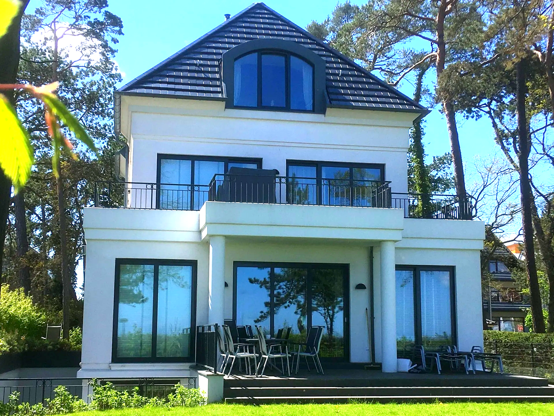 Ein großes weißes Haus mit einem schwarzen Dach ist von Bäumen umgeben