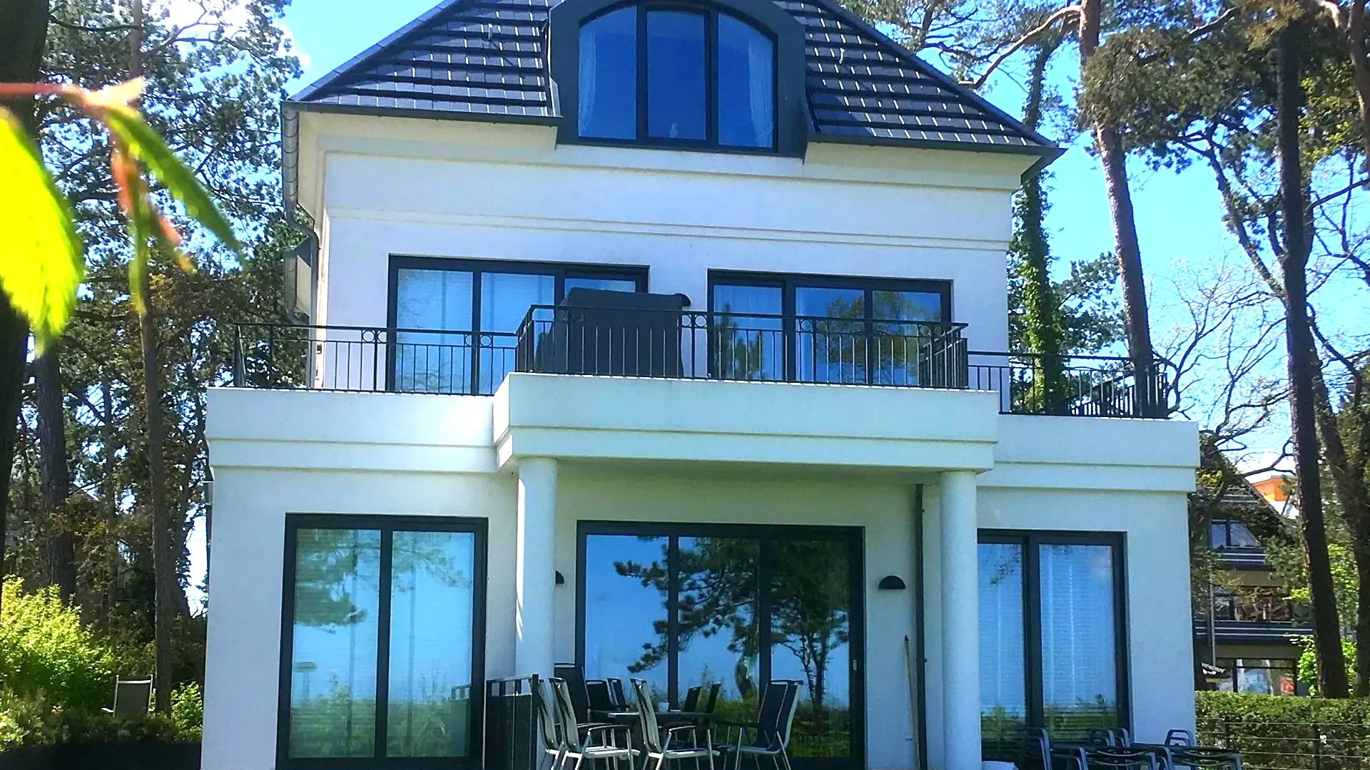 Ein großes weißes Haus mit Balkon ist von Bäumen umgeben