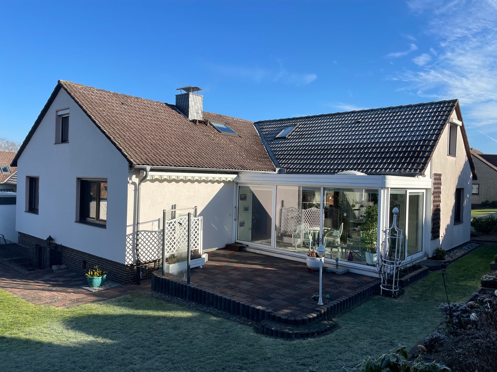 Ein weißes Haus mit einem braunen Dach und einer Terrasse davor.