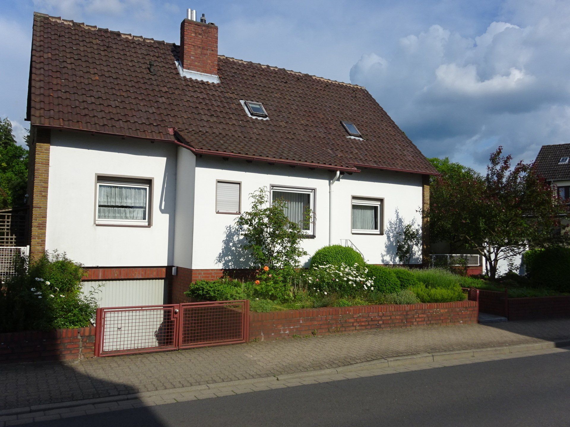 Ein weißes Haus mit einem braunen Dach und einem roten Tor