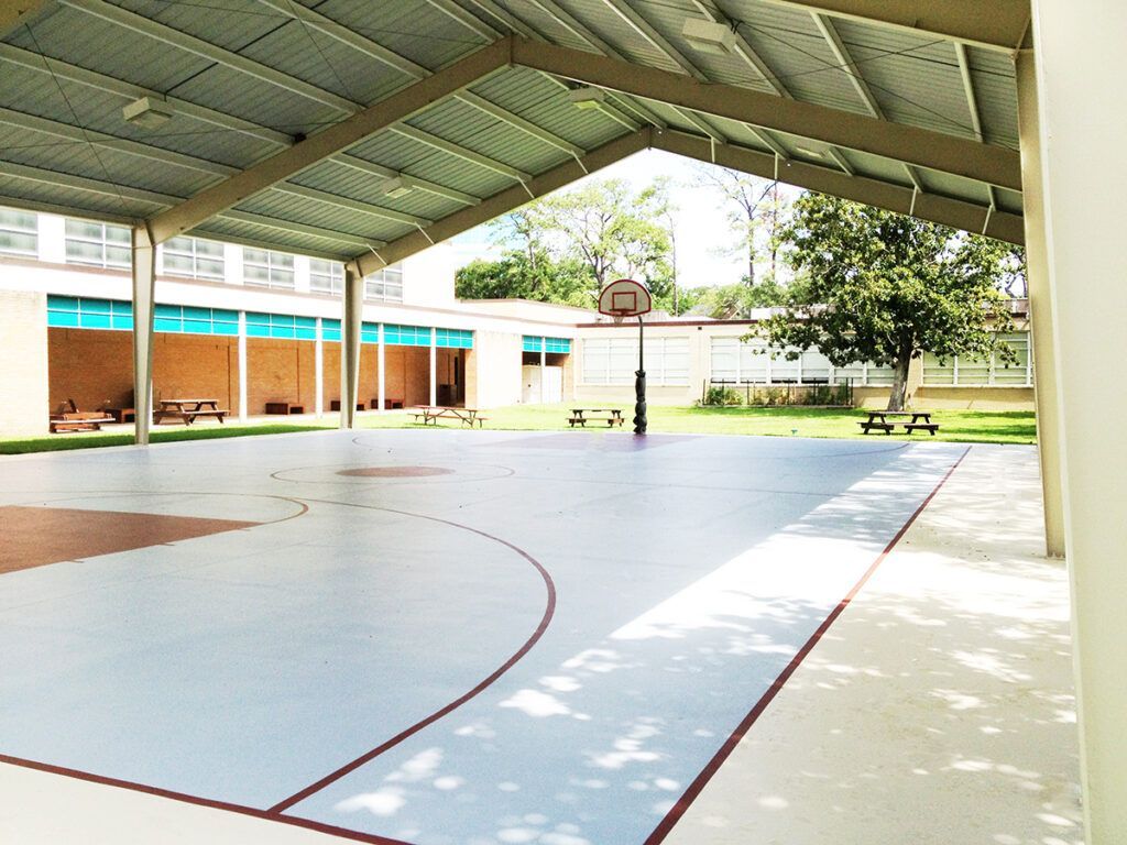 Covered basketball court with hoop, picnic tables, and school building in background.