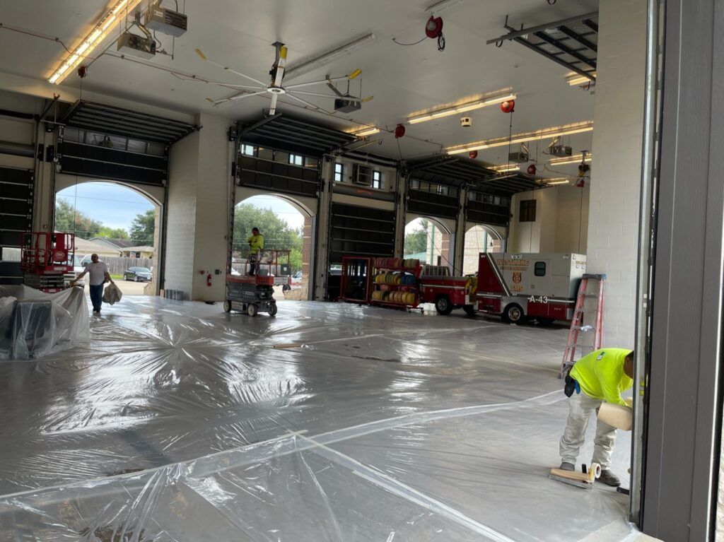 Interior of a fire station under construction. Workers are present near equipment and vehicles.