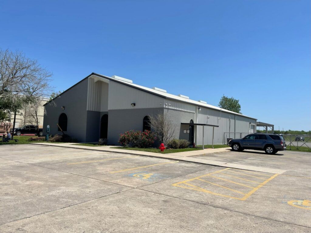 Gray industrial building with arched windows, parked SUV, blue sky, and concrete parking.