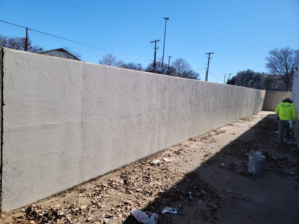 Concrete wall alongside a narrow path with a person in a safety vest.