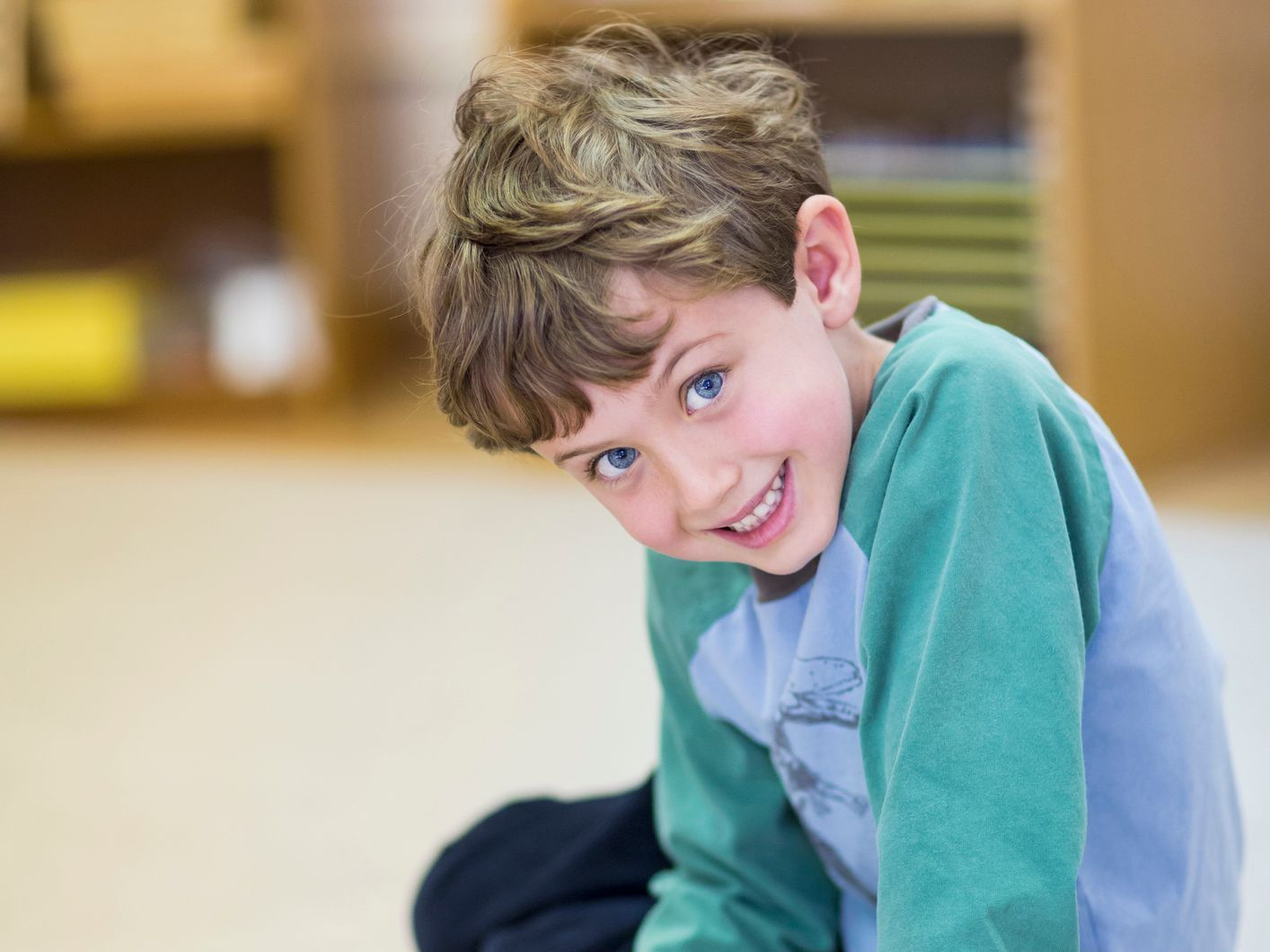 A young boy is sitting on the floor smiling for the camera.