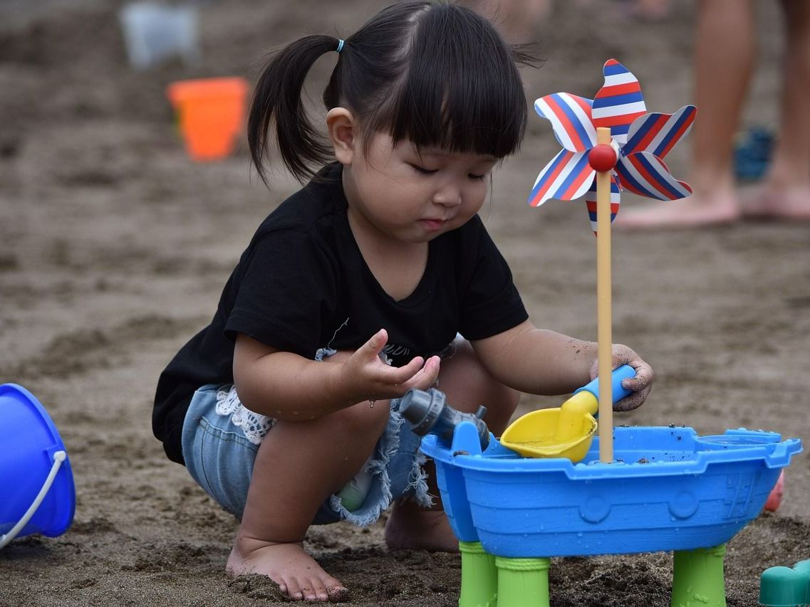A little girl is playing in the sand with a windmill.