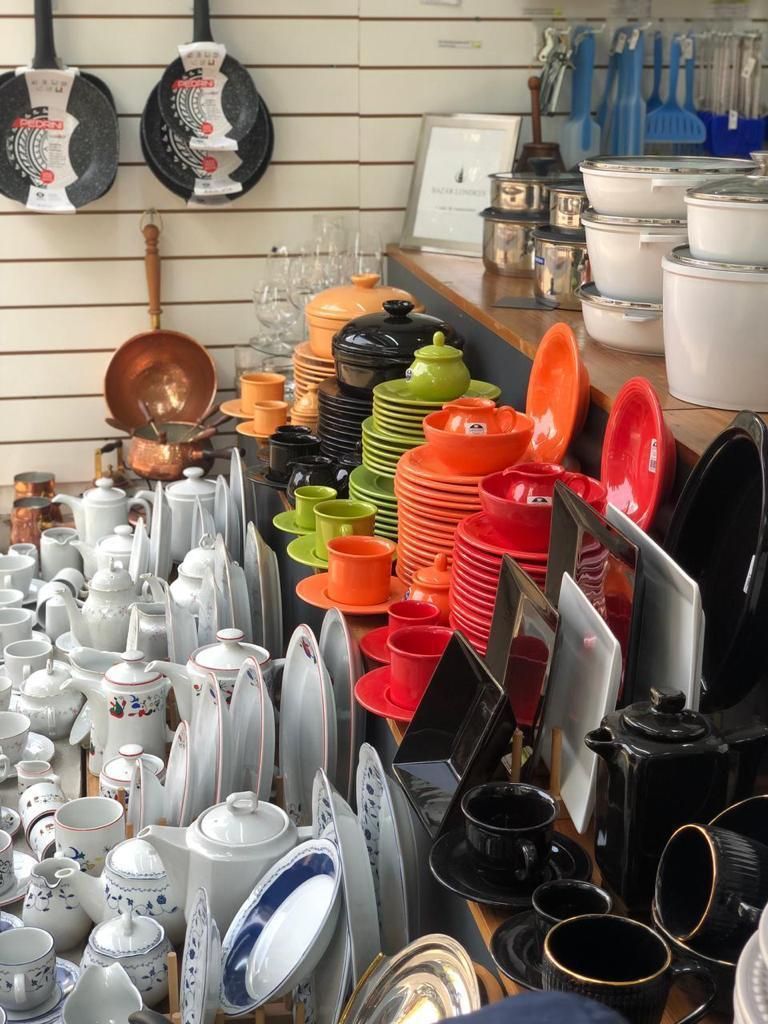 Exhibición de platos y utensilios de cocina coloridos en una tienda, incluidos platos, cuencos, tazas y ollas.