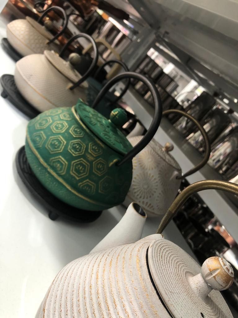 Teteras con dibujos verdes y blancos en exposición, con asas negras.