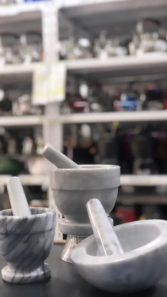 Tres juegos de mortero y maja de mármol sobre una mesa, con estantes con utensilios de cocina en el fondo.