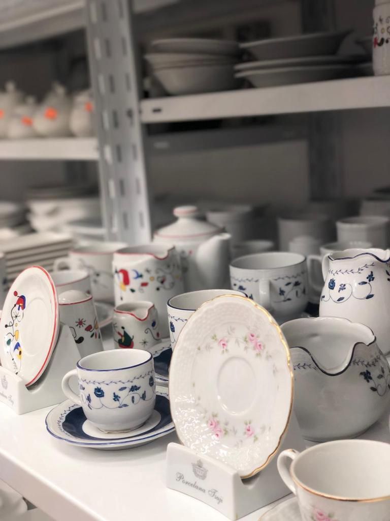 Estantes con diversas tazas de té, platillos y jarras de porcelana blanca, algunas decoradas con diseños azules y rosas.