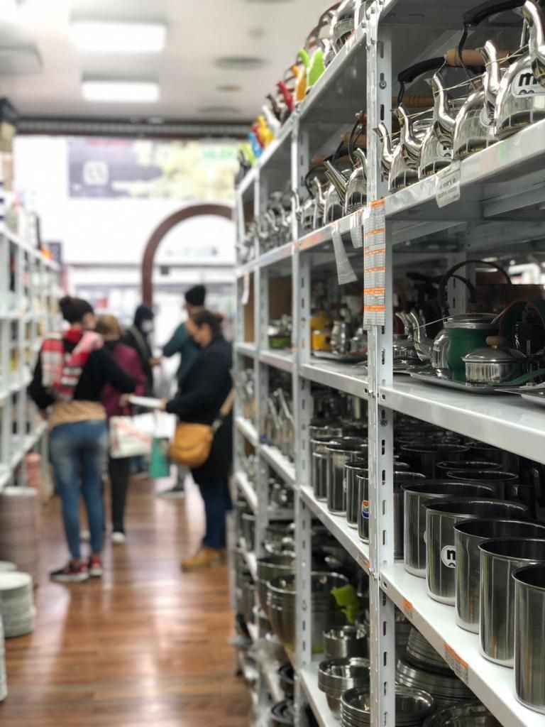 Estantes repletos de utensilios de cocina de metal en el pasillo de una tienda; la gente mira al fondo.