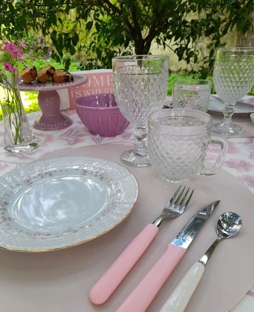 Elegante mesa de exterior con detalles en rosa y blanco. Incluye vajilla, comida y vasos.