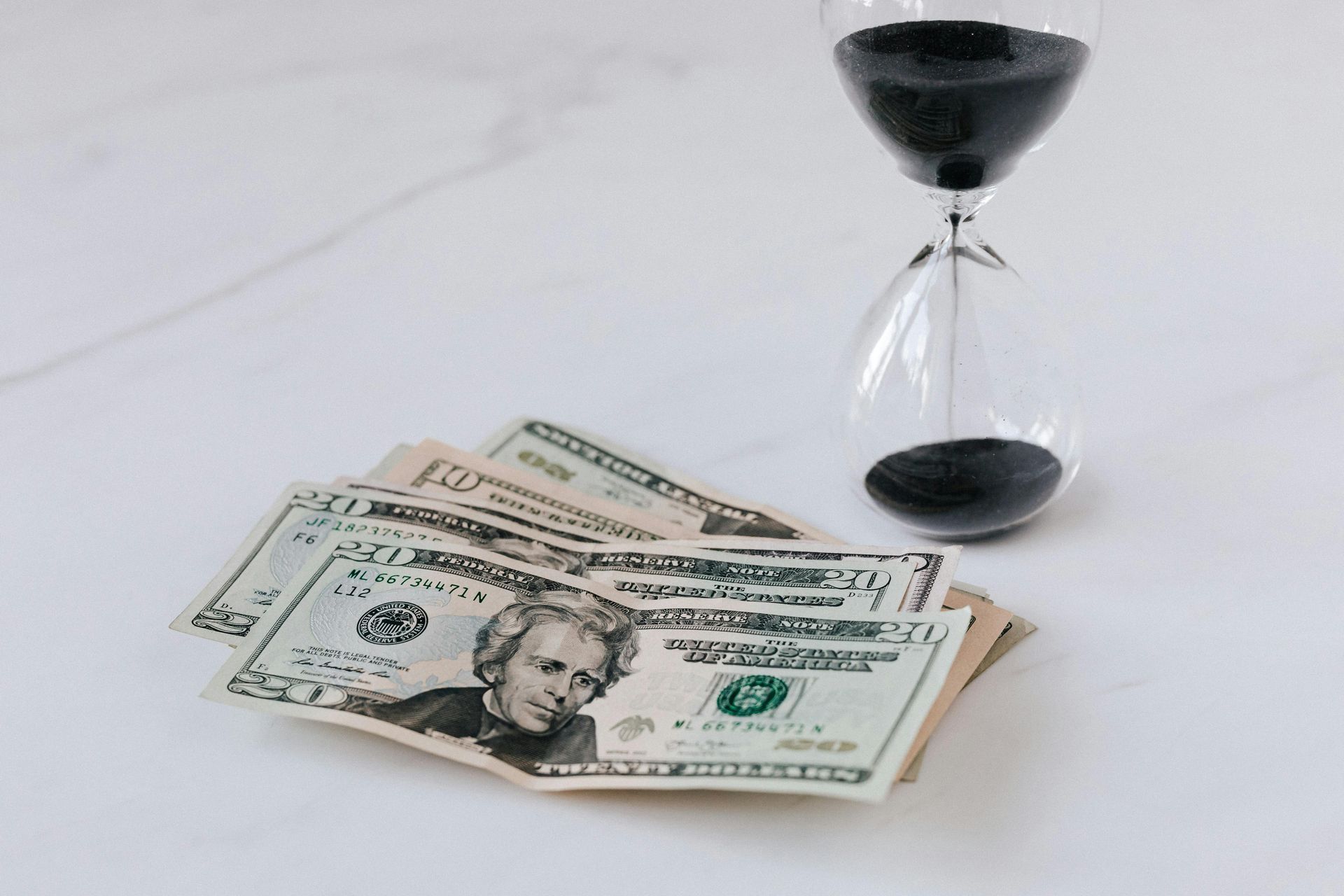 A hourglass is sitting next to a pile of money on a table.