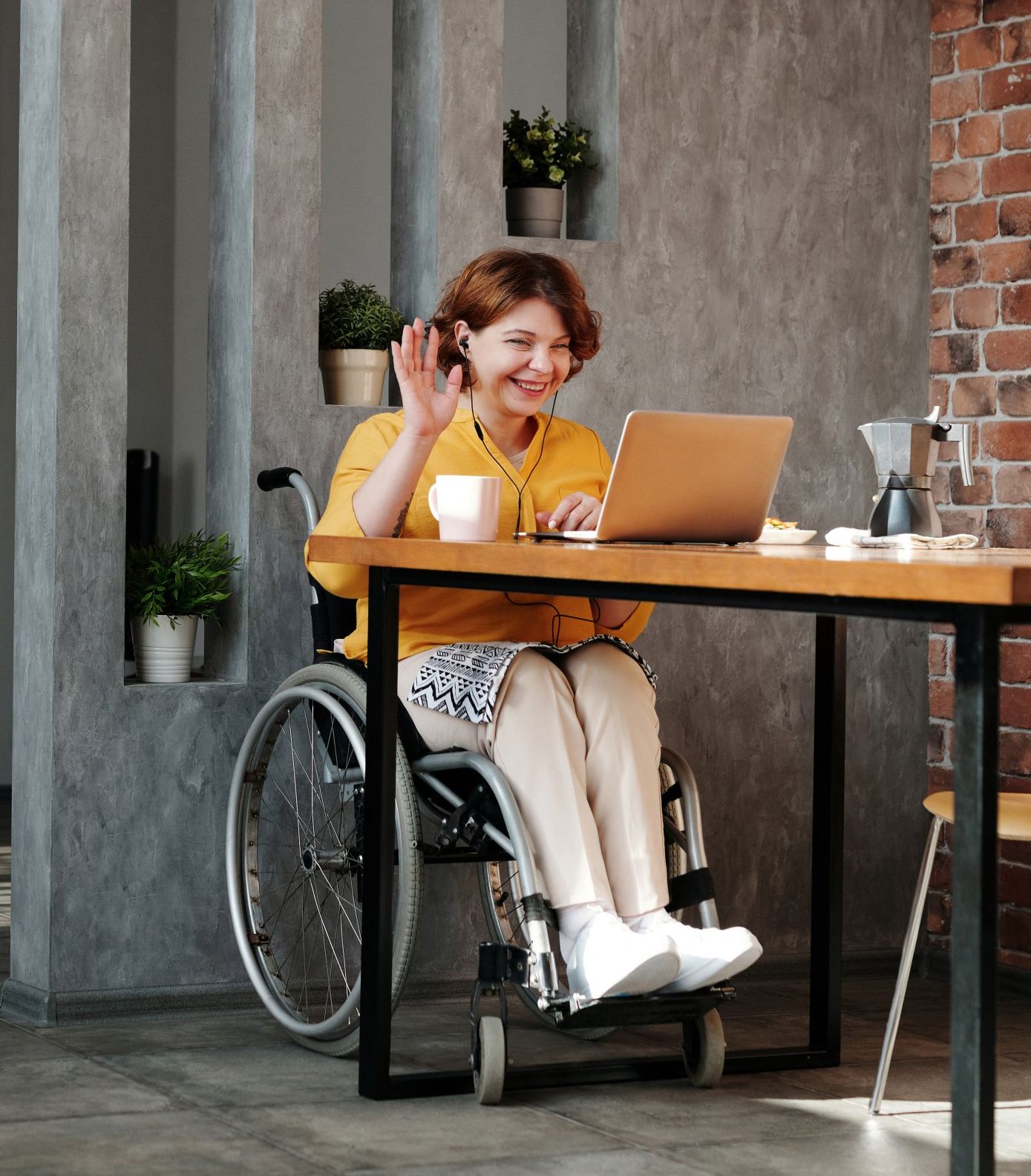 A woman in a wheelchair is sitting at a table with a laptop.