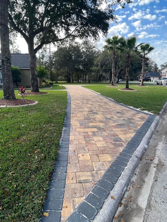A brick walkway leading to a house with palm trees in the background.
