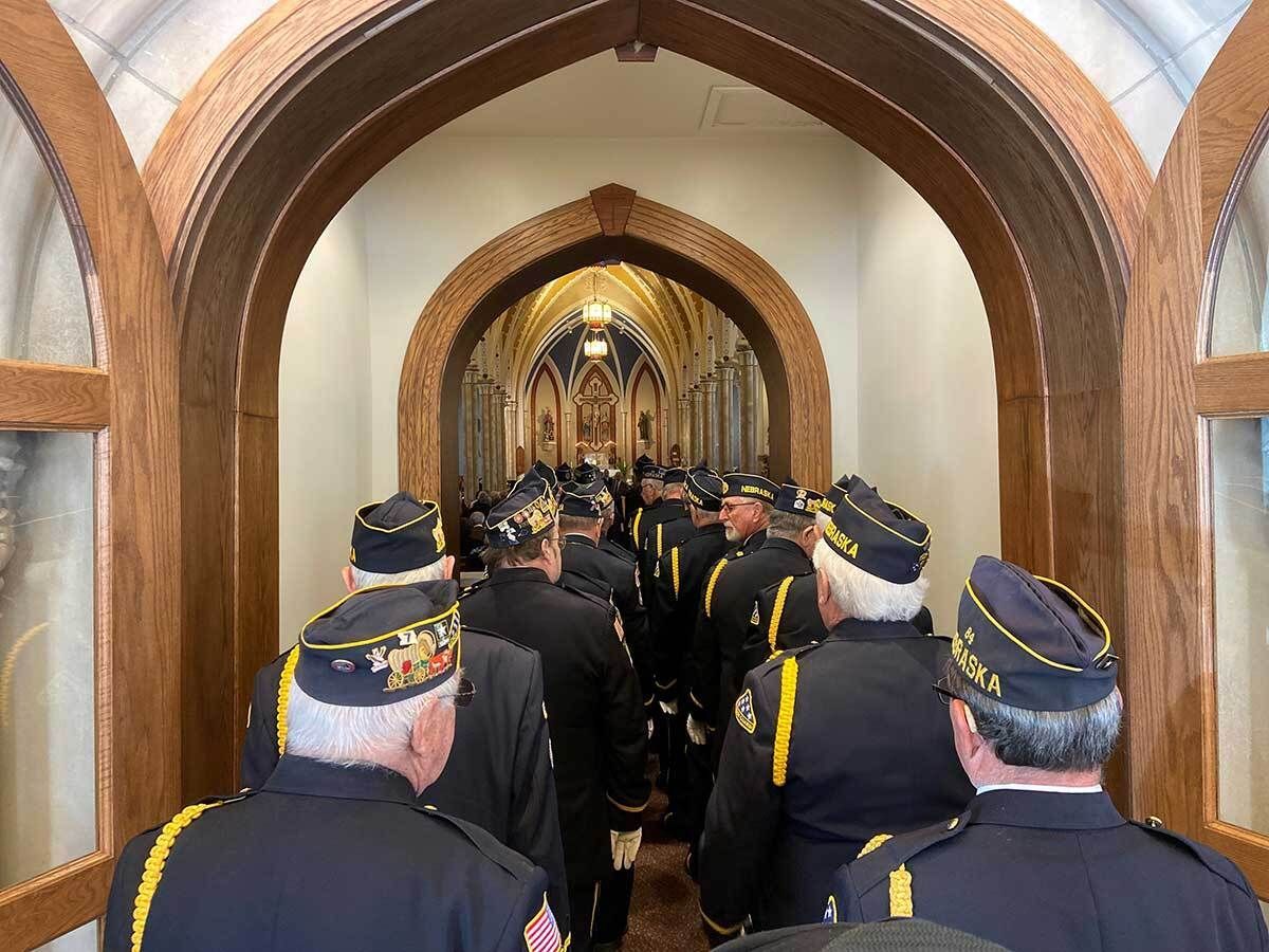 Veterans in uniform walking through a long arched hallway with ornate ceiling.