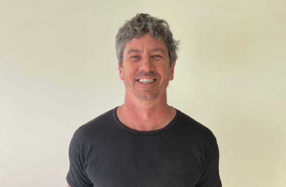 A young man in a blue sweater is smiling and looking at the camera.